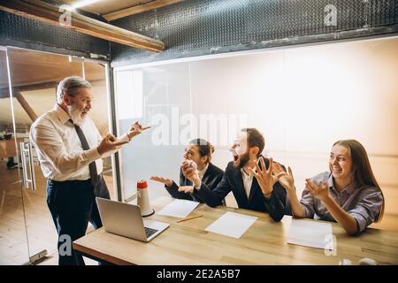 Beängstigend. Wütender Chef mit Megaphon, das Mitarbeiter im Büro anschreit, verängstigte und verärgerte Kollegen, die gestresst am Tisch zuhören. Witziges Meeting, Business, Bürokonzept. Schreiender Wahnsinn. Stockfoto