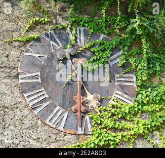 Eine alte Metalluhr auf einer rustikalen Wand eine alte Uhr auf der Mauer, die die Festung in Novi Sad umgibt. Serbien. Uhr mit Efeublättern. Stockfoto