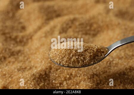 Braune Rohrzucker Kristalle in einem Löffel über Zucker Hintergrund. Gesunde Ernährung Süßigkeiten. Stockfoto