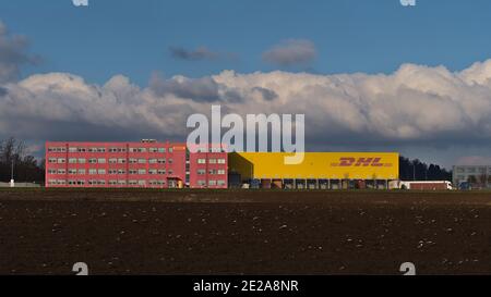 Vorderansicht des pinkfarbenen und gelben Logistikzentrums des Transportunternehmens DHL Global Forwarding, das zur Deutsche Post DHL Group gehört, mit Business-Logo. Stockfoto