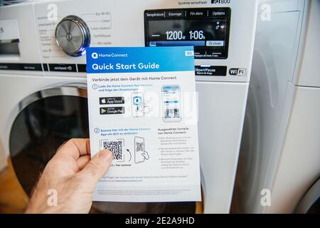 Paris, Frankreich - Jan 5, 2020: POV männliche Hand hält Bosch Home Connect Kurzanleitung mit zwei neuesten Siemens Wasch- und Trocknungsmaschine im Hintergrund Stockfoto