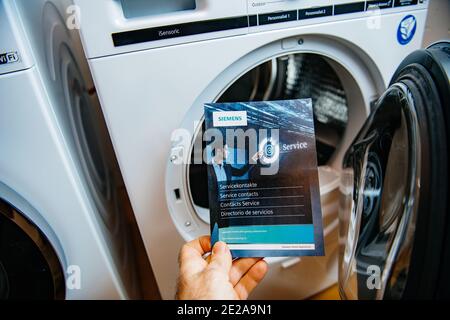 Paris, Frankreich - 5. Jan 2020: POV männliche Hand hält Bosch Service Kontakt Flyer Werbeinformatio Guide mit zwei neuesten Siemens Wasch- und Trocknungsmaschinen im Hintergrund Stockfoto