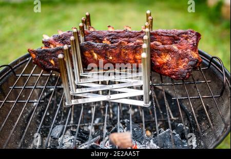Baby zurück Spare Ribs Braten auf BBQ Grill Kugelgrill. Hausgemachte Schweinerippchen auf einem Grill mit geringe und langsame Methode. Grillen draußen in der Natur bei Fami Stockfoto