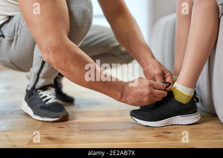 Ein kurzer Schnitt von Papa, der die Schnürsenkel an einem Kinder-Sneaker bindet, während er sich für das Training zu Hause vorbereitet. Konzept der Familie Stockfoto