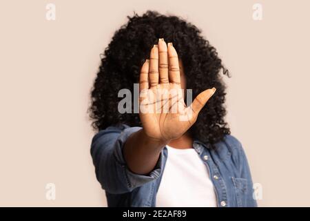 Schwarze Frau zeigt ihre Handfläche und versteckt das Gesicht vor der Kamera Stockfoto