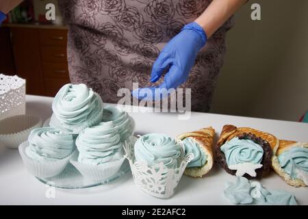 Frau in Gummihandschuhen macht Marshmallows. In der Nähe befindet sich ein zephyr in einem Waffelkegel. Dessert liegt auf der Tischoberfläche. Stockfoto