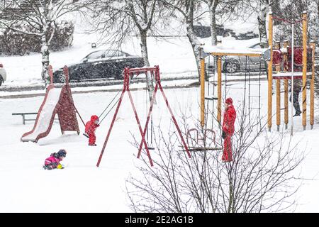 Wunderschöne weiße Winterlandschaft mit Bäumen, die von Schnee bedeckt sind Schneefall mit Kindern und Mutter spielen auf dem Spielplatz Stockfoto