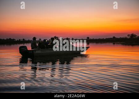 Menschen auf dem Boot, die den Sonnenuntergang im Okavango Delta betrachten. Stockfoto