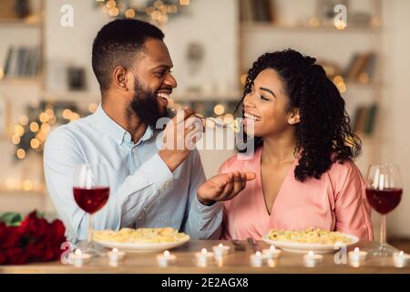 Lächelnder schwarzer Mann füttert seine glückliche Frau mit Pasta Stockfoto