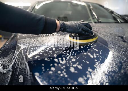 Mann reinigt Autohaube mit Kreis Schwamm. Automatische Vorbereitung für das Polieren. Detaillierte Autowäsche Stockfoto