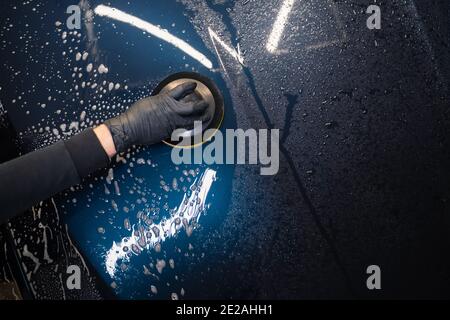 Mann reinigt Autohaube mit Kreis Schwamm. Automatische Vorbereitung für das Polieren. Detaillierte Autowäsche Stockfoto