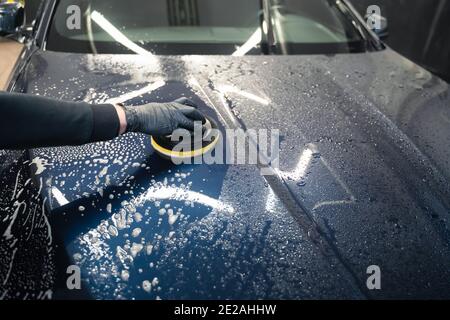 Mann reinigt Autohaube mit Kreis Schwamm. Automatische Vorbereitung für das Polieren. Detaillierte Autowäsche Stockfoto