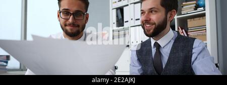 Lächelnde Männer am Computer halten in Waffen Finanzpapiere Stockfoto