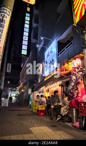 Setagaya, Tokio, Japan - September 27 2020: Einige Gäste genießen Getränke direkt vor einer gut beleuchteten Bar in einer engen Gasse im Südwesten Tokios Stockfoto