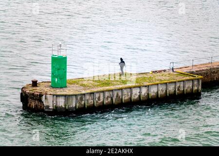 Einsamer Angler, der auf einem Pier am Meer steht. Stockfoto