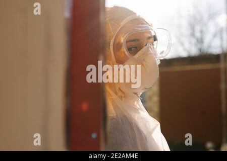 Portraitfoto eines Arztes in Schutzausrüstung, lehnte sich an die Wand vor dem Hintergrund der Außensonne. Das Konzept der Bekämpfung des Virus. Stockfoto