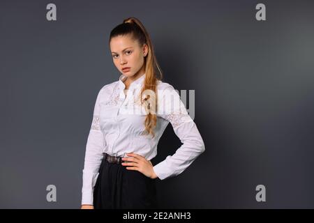 Junge seriöse Geschäftsfrau posiert über grauen Hintergrund mit leeren Seitenraum. Stockfoto
