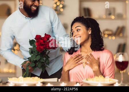 Junger schwarzer Mann, der der aufgeregten Frau rote Rosen gibt Stockfoto