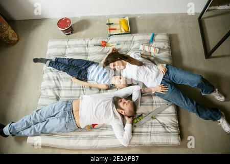 Junges Paar, Familie tun Wohnung Reparatur zusammen selbst. Mutter, Vater und Sohn tun zu Hause Verjüngungskur oder Renovierung. Konzept der Beziehungen, Bewegung, Liebe. Auf Matratze ruhen, Draufsicht Stockfoto