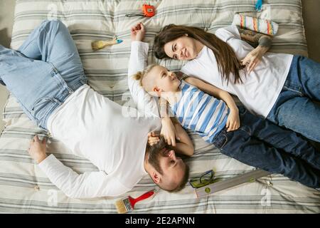 Junges Paar, Familie tun Wohnung Reparatur zusammen selbst. Mutter, Vater und Sohn tun zu Hause Verjüngungskur oder Renovierung. Konzept der Beziehungen, Bewegung, Liebe. Auf Matratze ruhen, Draufsicht Stockfoto