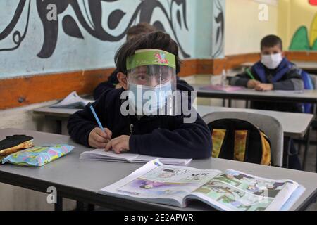 (210113) -- GAZA, 13. Januar 2021 (Xinhua) -- EIN palästinensischer Student, der eine Gesichtsmaske und einen Gesichtsschutz trägt, besucht nach seiner Wiedereröffnung als COVID-19-Beschränkungsmaßnahme eine Klasse in Gaza-Stadt, 13. Januar 2021. (Foto von Rizek Abdeljawad/Xinhua) Stockfoto