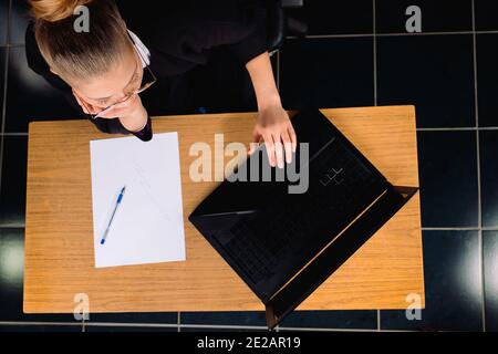 Foto von oben. Geschäftsfrau sitzt an einem Computer im Büro mit Dokumenten auf dem Tisch. Stockfoto