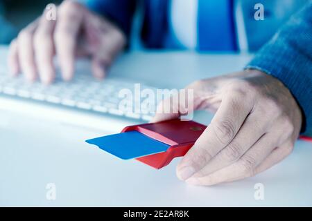 Nahaufnahme eines jungen Kaukasiers, der einen eleganten blauen Anzug trägt, an der Rezeption mit einem roten Zahlungsterminal und einer blauen Kreditkarte Stockfoto