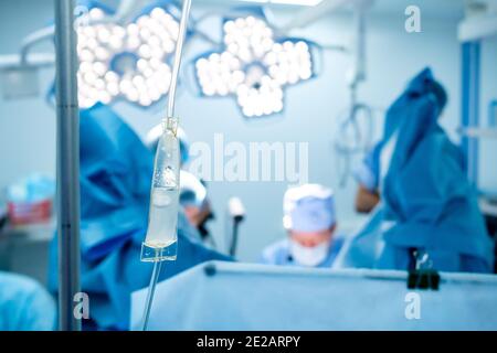 Transparente Kunststoffröhrchen und Pipette für einen medizinischen Tropf mit Kochsalzlösung. Vor einem sehr verschwommenen Hintergrund führen Chirurgen eine Operation durch Stockfoto