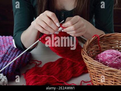 Junge Frau strickt roten Schalldämpfer zu Hause in der Freizeit, Fancywork und Nadelarbeit Konzept, Nahaufnahme der Handarbeit, Kopierraum, von oben Ansicht von oben Stockfoto