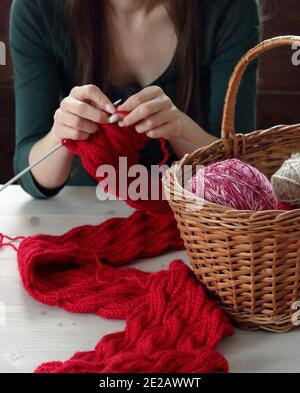 Junge Frau strickt roten Schalldämpfer zu Hause in der Freizeit, Fancywork und Nadelarbeit Konzept, Nahaufnahme der Handarbeit, Kopierraum, von oben Ansicht von oben Stockfoto