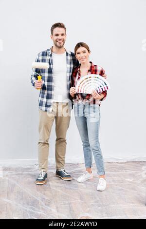 Voller Länge lächelnden jungen Mann mit Farbe Roller umarmt Frau zeigt Farbpalette zu Hause Stockfoto