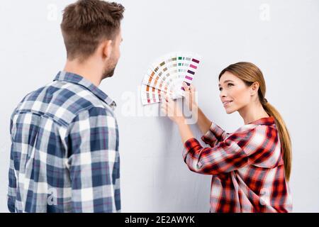 Lächelnde junge Frau, die den Mann anschaut, während sie mit dem Finger zeigt Bei Farbpalette im Innenbereich Stockfoto