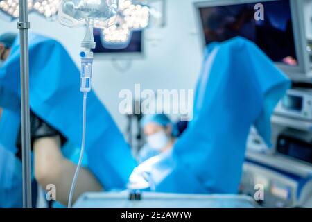 Transparente Kunststoffröhrchen und Pipette für einen medizinischen Tropf mit Kochsalzlösung. Vor einem sehr verschwommenen Hintergrund führen Chirurgen eine Operation durch Stockfoto