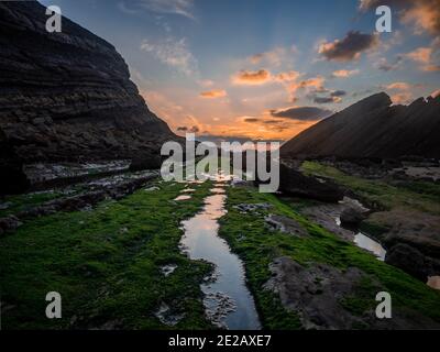 Schöne Landschaft bei Sonnenuntergang vom Madero Strand in Liencres, Kantabrien. Wasserwege und Felsen mit grünem Moos bedeckt Stockfoto