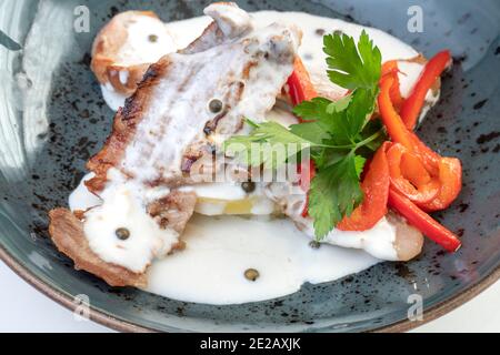 Iberisches Geheimnis mit Pfeffersauce, Petersilie und Gemüse, auf einem dunkelblauen Teller Stockfoto