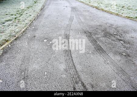 Nahaufnahme der Reifenspuren auf vereisten Straßen mit Im Winter nach einem harten Frost ragt das Gras nach draußen Stockfoto