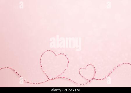 Valentinskarte. Herzformen aus rot weißem Faden oder Seil. Rosa Hintergrund Stockfoto