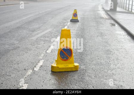 Nahaufnahme der gelben Warnung, keine wartenden Verkehrskegel, auf asphaltierten Straße, die den Verkehr an einem nebligen Tag nicht zum Parken am Straßenrand leitet Stockfoto