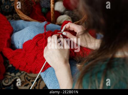 Junge Frau strickt roten Schalldämpfer zu Hause in der Freizeit, Fancywork und Nadelarbeit Konzept, Nahaufnahme der Handarbeit, Kopierraum, von oben Ansicht von oben Stockfoto