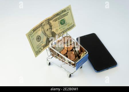 Einkaufswagen voller Münzen, amerikanische 20-Dollar-Banknote Geld und ein Smartphone.Shopping-Konzept, E-Commerce, Business-Marketing, Supermarkt tro Stockfoto