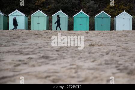 Am Bournemouth Beach in Drset laufen die Leute vorbei an Strandhütten. Stockfoto