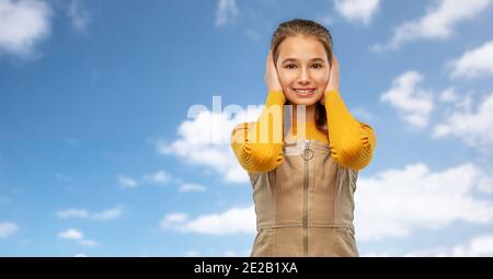 Lächelndes Teenager-Mädchen, das die Ohren über dem Himmel schließt Stockfoto