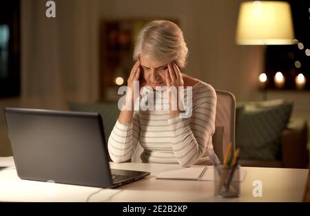 Müde ältere Frau mit Laptop zu Hause in der Nacht Stockfoto