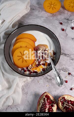 Gesundes Essen, Frühstück, frisches Kaki mit Granatapfel und Haferflocken, wunderschön auf einem Marmortisch arrangiert Stockfoto