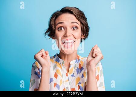 Foto von glücklich erstaunt triumphierenden Mädchen heben Fäuste tragen weiß Print Shirt isoliert auf blauem Hintergrund Stockfoto