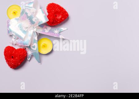 Roter Geschenkbogen und leuchtende Duftkerzen in Form von roten Herzen auf ultimativ grauem frn mit Platz an der Seite. Stockfoto