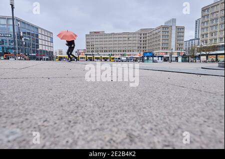 Berlin, Deutschland. Januar 2021. Eine Frau mit einem Sonnenschirm läuft über den Alexanderplatz. Sonst gibt es Leere auf dem Platz. Quelle: Annette Riedl/dpa/Alamy Live News Stockfoto