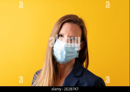 Porträt einer jungen Geschäftsfrau mit medizinischer Schutzmaske. Auf gelbem Hintergrund. Stockfoto