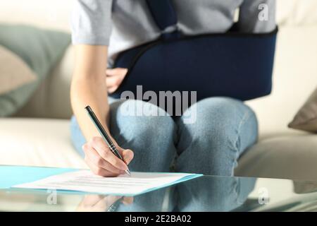 Vorderansicht einer behinderten Frau mit Schlinge bei Vertragsunterzeichnung Zu Hause Stockfoto