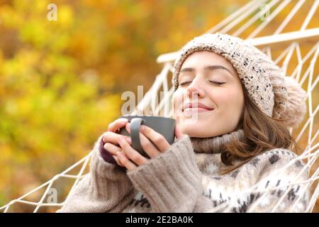 Entspannte Frau, die Kaffee riecht, liegt in den Herbstferien in der Hängematte Stockfoto